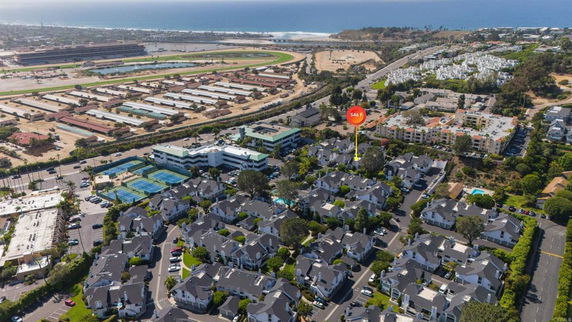 Aerial view of a residential neighborhood with nearby tennis courts, buildings, and a water body in the distance.
