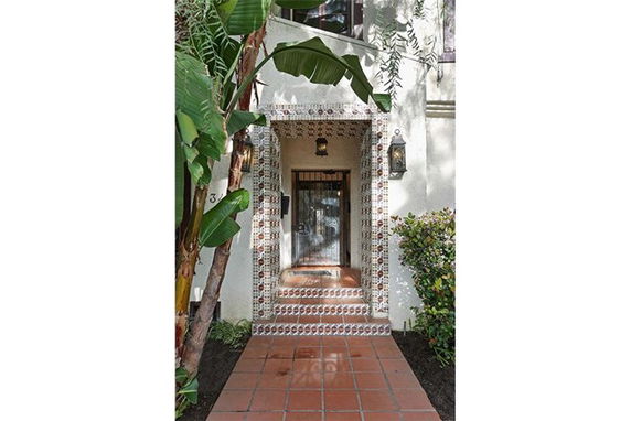 Entrance view of a house with decorative tile framing and a small porch, surrounded by plants.
