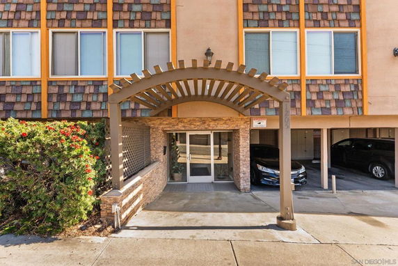 Front view of a building entrance with a wooden archway and parking spaces.