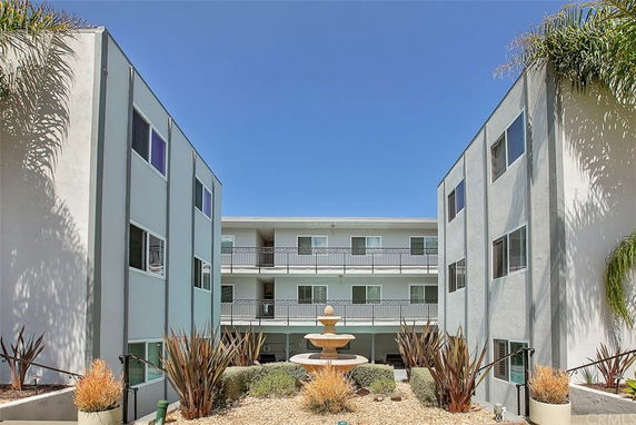 Front elevation of a three-story building with balconies and a central courtyard featuring a fountain.