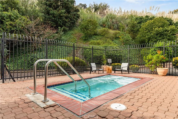 Outdoor swimming pool area with adjacent seating surrounded by greenery.