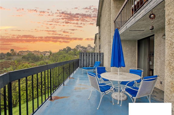 Outdoor patio with a table, chairs, and umbrella, overlooking a scenic landscape at sunset.