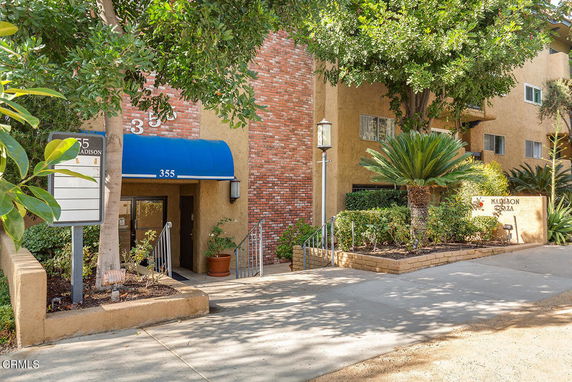 Front view of a multi-story building with a brick and stucco facade, blue awning, and landscaped entrance.