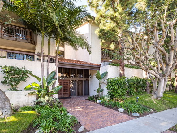 Front view of a multi-story building with balconies and greenery at the entrance.