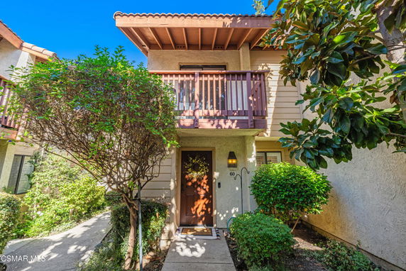 Front view of a two-story house with a wooden balcony and decorative plants.