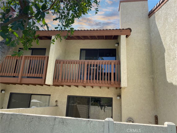 Front view of a two-story house with balconies and light-colored walls.