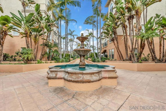 Outdoor courtyard with a central water fountain surrounded by palm trees and building facades.