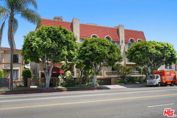 Front view of a multi-story apartment building with a red-tiled roof and balconies.