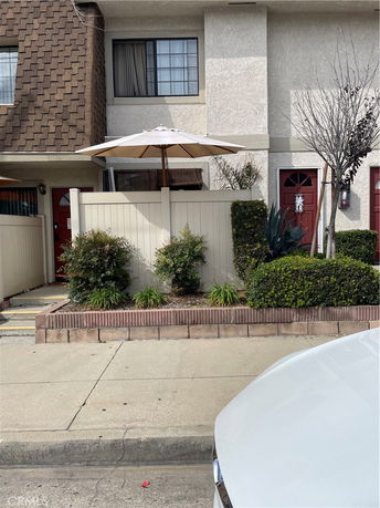 Front view of a townhouse with a small patio and red doors.
