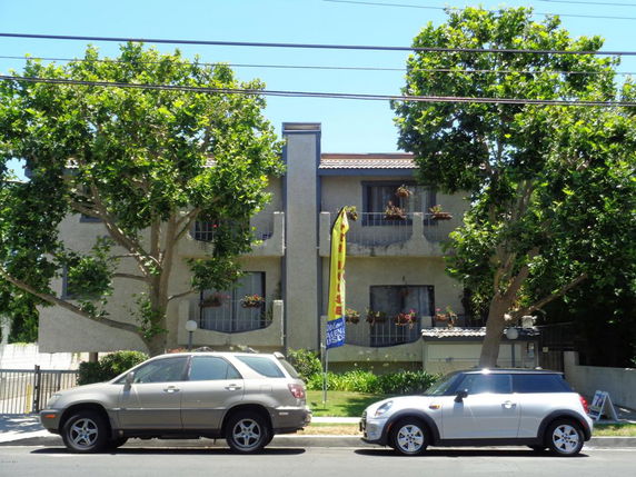 Front view of a multi-story residential building with balconies and trees in front.