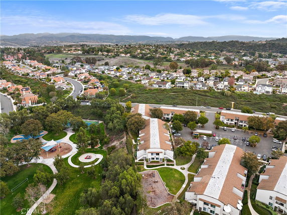 Panoramic view of residential area with houses, greenery, and hills in the background.