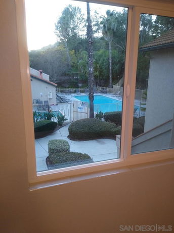 View of a swimming pool and surrounding area from a window, with trees and a building nearby.