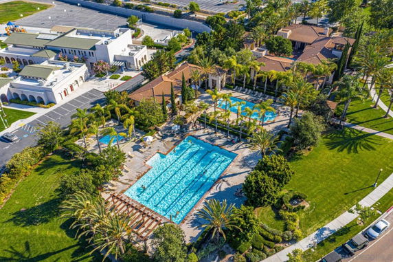Aerial view of an outdoor swimming pool complex with surrounding greenery and nearby buildings.