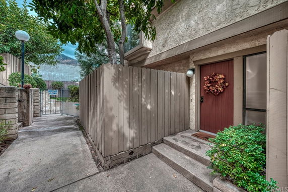 Front view of a beige two-story building entrance with a wooden door and fence.