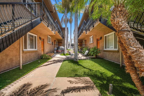 Outdoor area between two apartment buildings with balconies and palm trees.