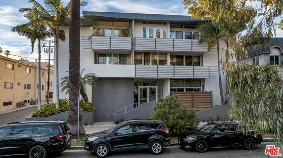 Front view of a multi-story residential building with balconies and palm trees.