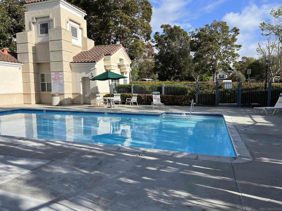 Outdoor swimming pool area with surrounding fence and chairs.