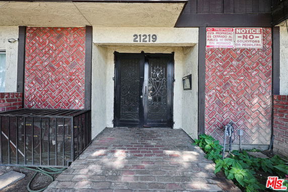 Front view of a building entrance with a decorative metal door and brick pattern walls.