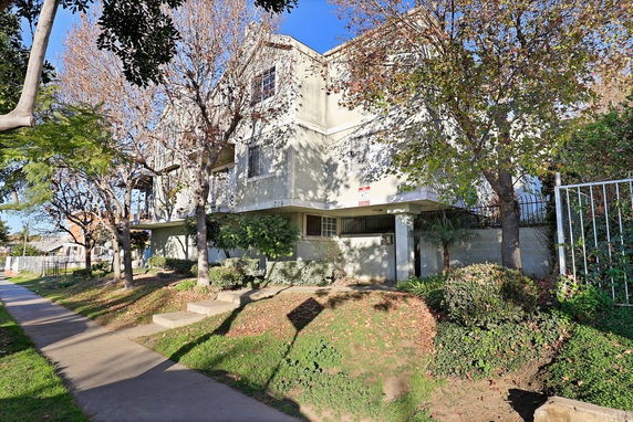 Front view of a multi-story residential building with trees along the sidewalk.