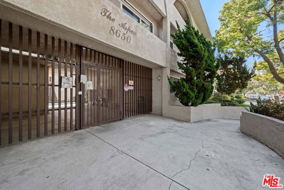 Front view of an apartment building with a gated entrance and greenery.