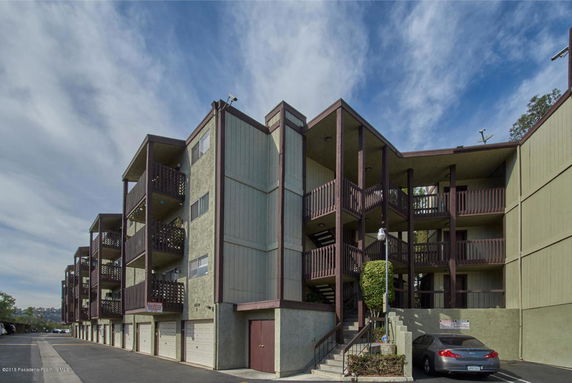 Front view of a multi-story apartment building with balconies and a parking area.