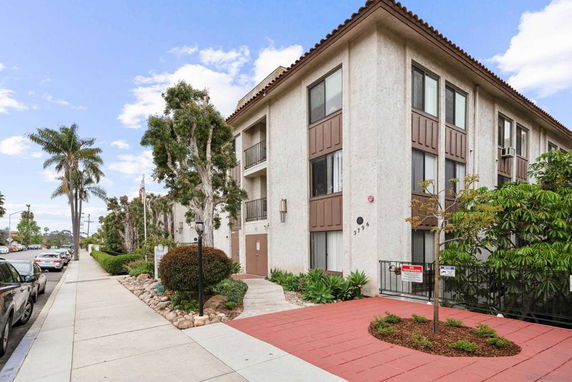 Front view of a multi-story apartment building with large windows and a red paving path.