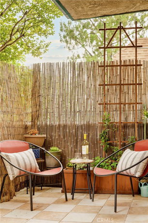 Outdoor patio area with two chairs, a small table with a bottle and glass, surrounded by bamboo fencing and potted plants.
