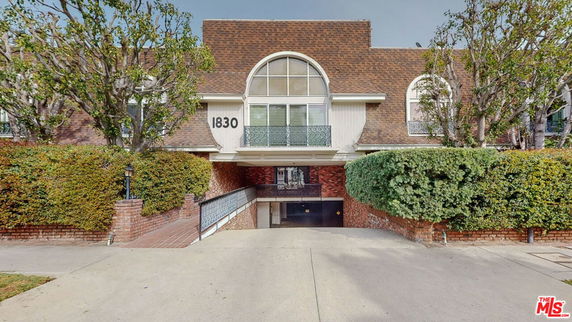 Front view of a multi-story building with a brick and brown facade, featuring arched windows and a gated entrance.