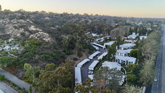 Aerial view of a residential area with multiple houses and roads surrounded by hilly and forested terrain.