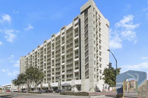Front view of a multi-story building with balconies and commercial spaces at street level.