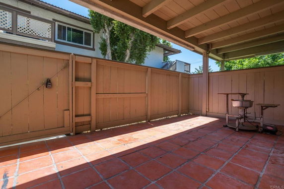 View from a covered patio with tiled flooring, showing a wooden fence and neighboring houses.
