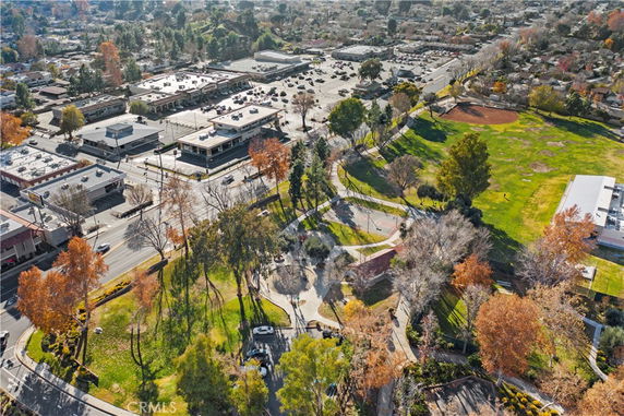 Aerial view showing a city landscape with commercial buildings, parking areas, roads, and a park with trees and pathways.