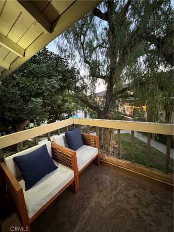 View from a balcony with wooden chairs, showing trees and nearby buildings.