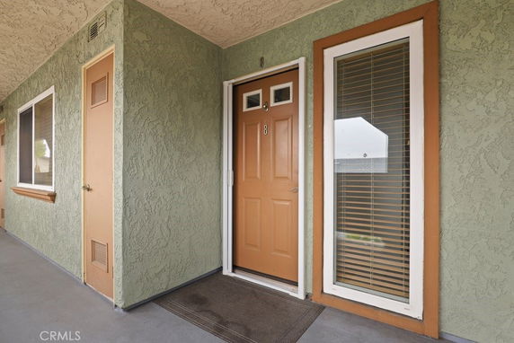 Exterior view of a house entrance with a brown door and adjacent window with blinds.