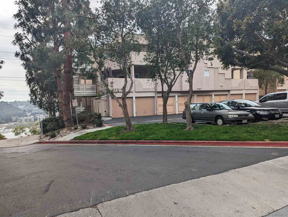 Outdoor parking area in front of a multi-story building with several vehicles parked.