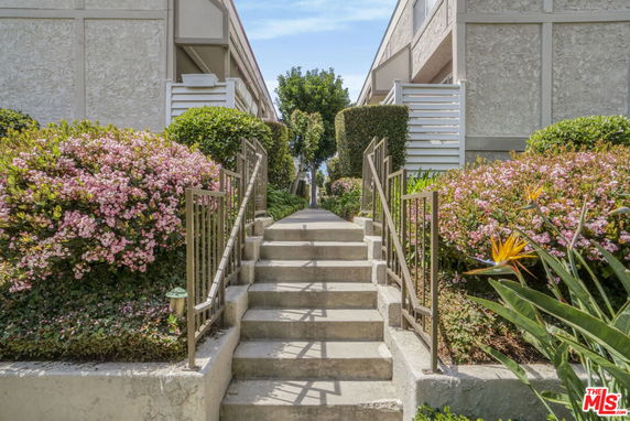 Front view of a building with stairs leading up to the entrance, flanked by flowering bushes.