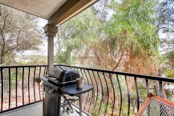 Balcony view with barbecue grill and trees in the background.