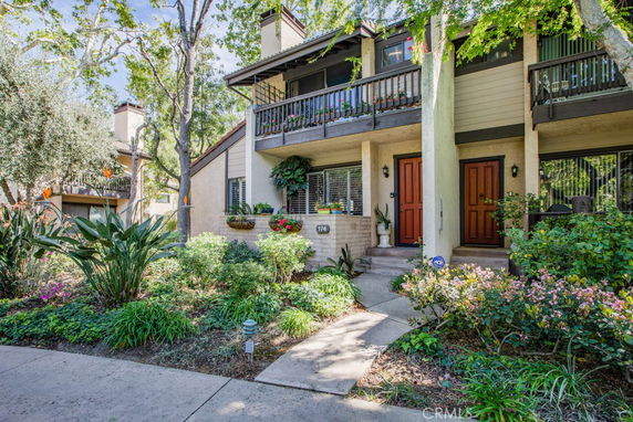 Front view of a two-story house with balconies and a lush garden.