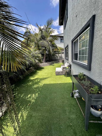 Side view of a house with an artificial grass yard and palm trees.