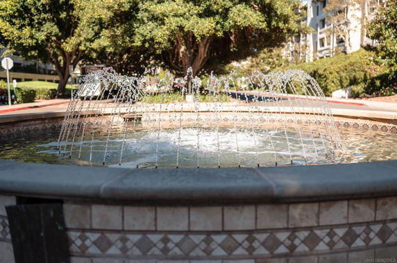 Decorative outdoor fountain with water jets, surrounded by tile in a landscaped area.