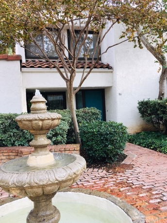 Front view of a two-story house with a tiled roof and a fountain.