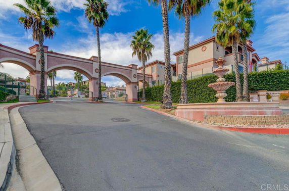 Front view of a gated residential complex with arches and palm trees.