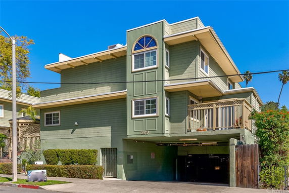 Front view of a multi-story green house with a balcony and an open garage area.