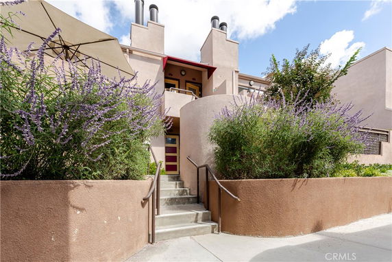 Front view of a two-story building with a prominent staircase and surrounding greenery.