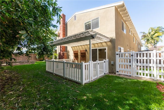Side view of a two-story house with a fenced patio and pergola.