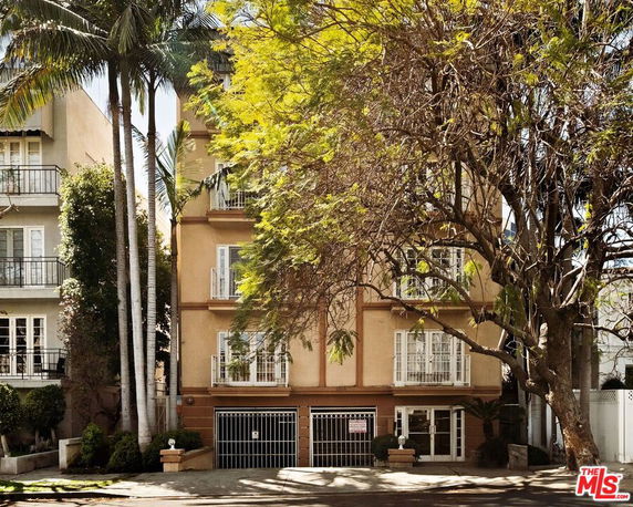 Front view of a multi-story residential building with multiple balconies and gated parking area.