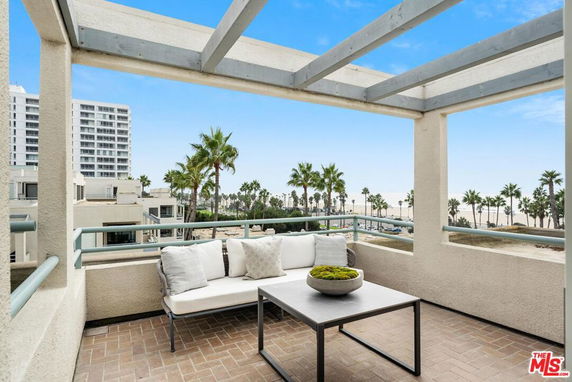 Outdoor terrace with a seating area and view of nearby buildings and palm trees.