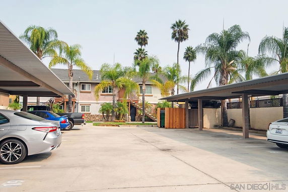 Outdoor parking area with covered parking spaces and several palm trees visible in the background.