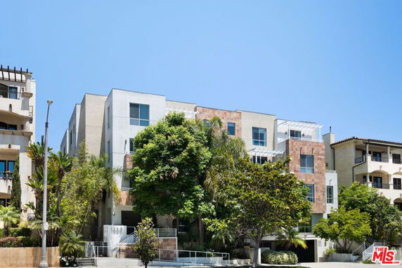 Front view of a modern multi-story residential building with trees in front.