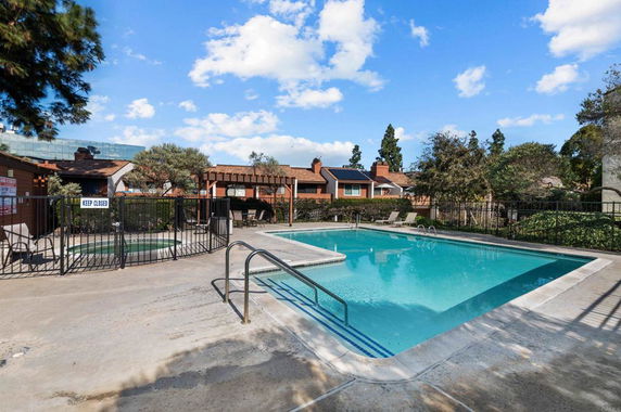 Outdoor swimming pool area with surrounding fence and nearby buildings.